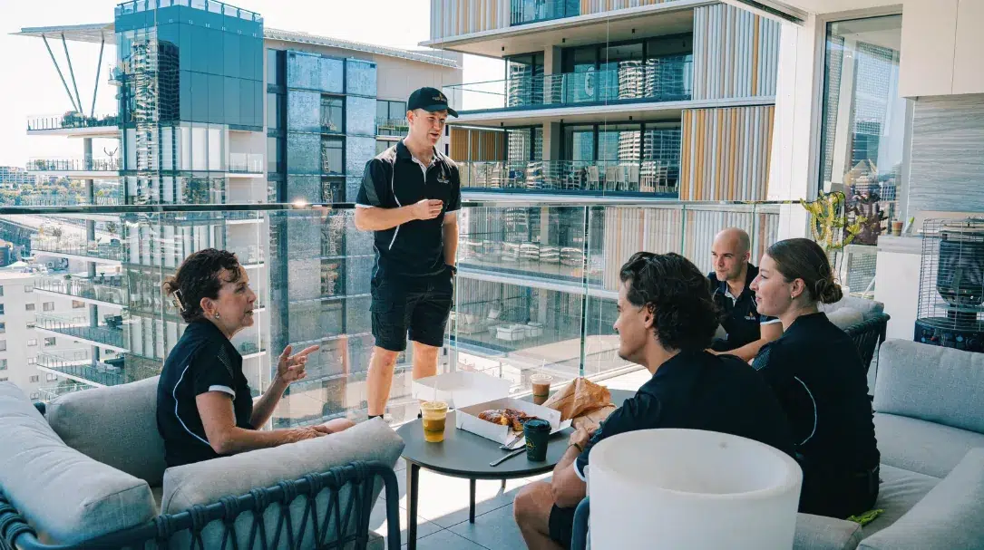 A small retained cleaning team in uniform meeting together over coffee on a high-rise apartment balcony.