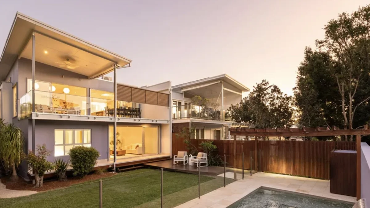 Two-storey modern home at dusk with lit interiors, a covered balcony, timber fencing and a plunge pool in the backyard.